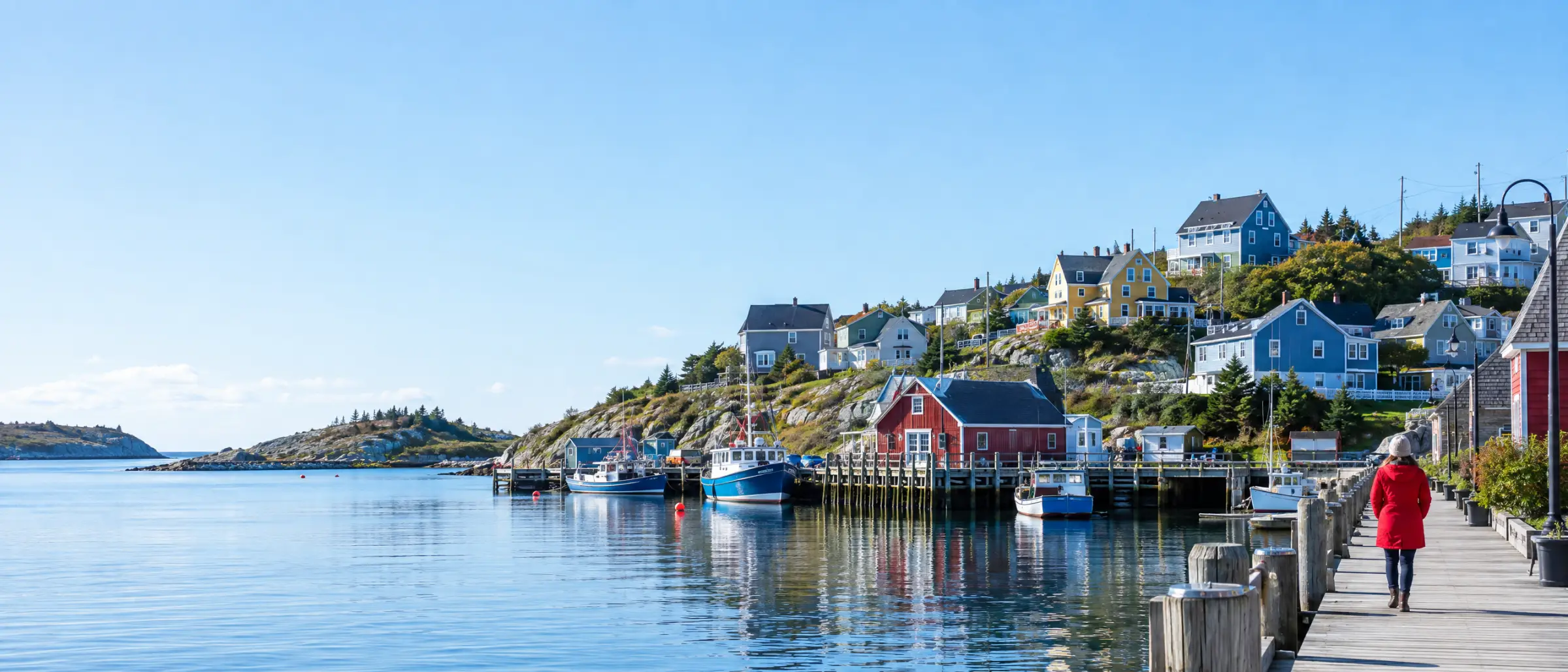 A small Atlantic Canadian harbour town on a sunny morning, a person in a red coat walking along the waterfront boardwalk